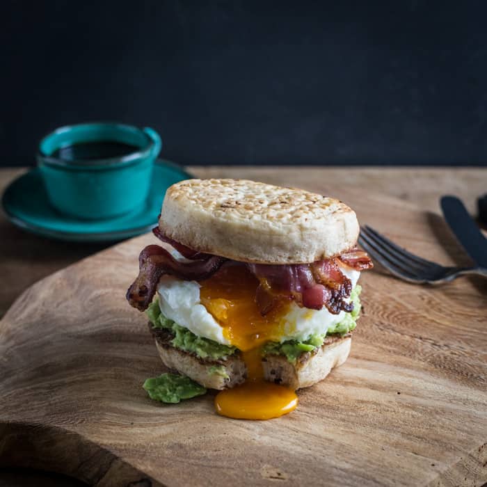 Breakfast Crumpet Burger on a wooden board with a knife and fork and a cup of coffee