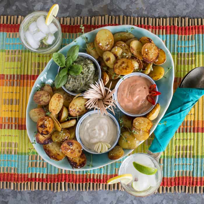 colourful background with blue plate filled with crispy fried potatoes and 3 bowls of flavoured mayo