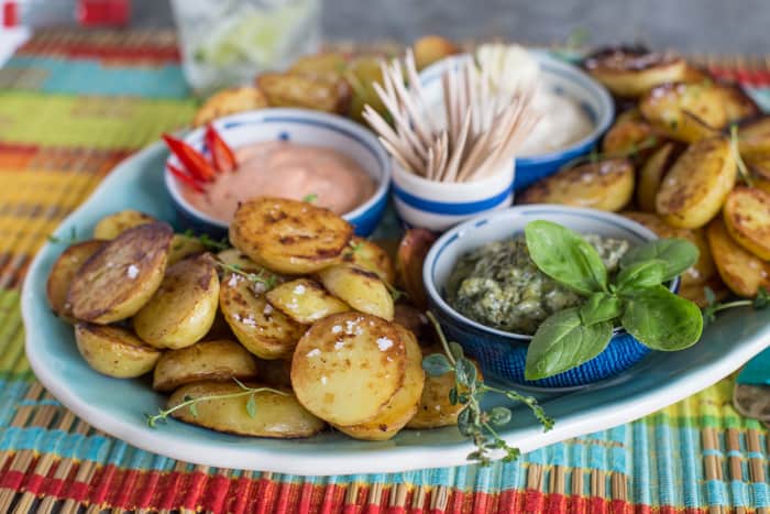 big plate of golden brown fried potatoes, and little bowls of red, green and white mayo