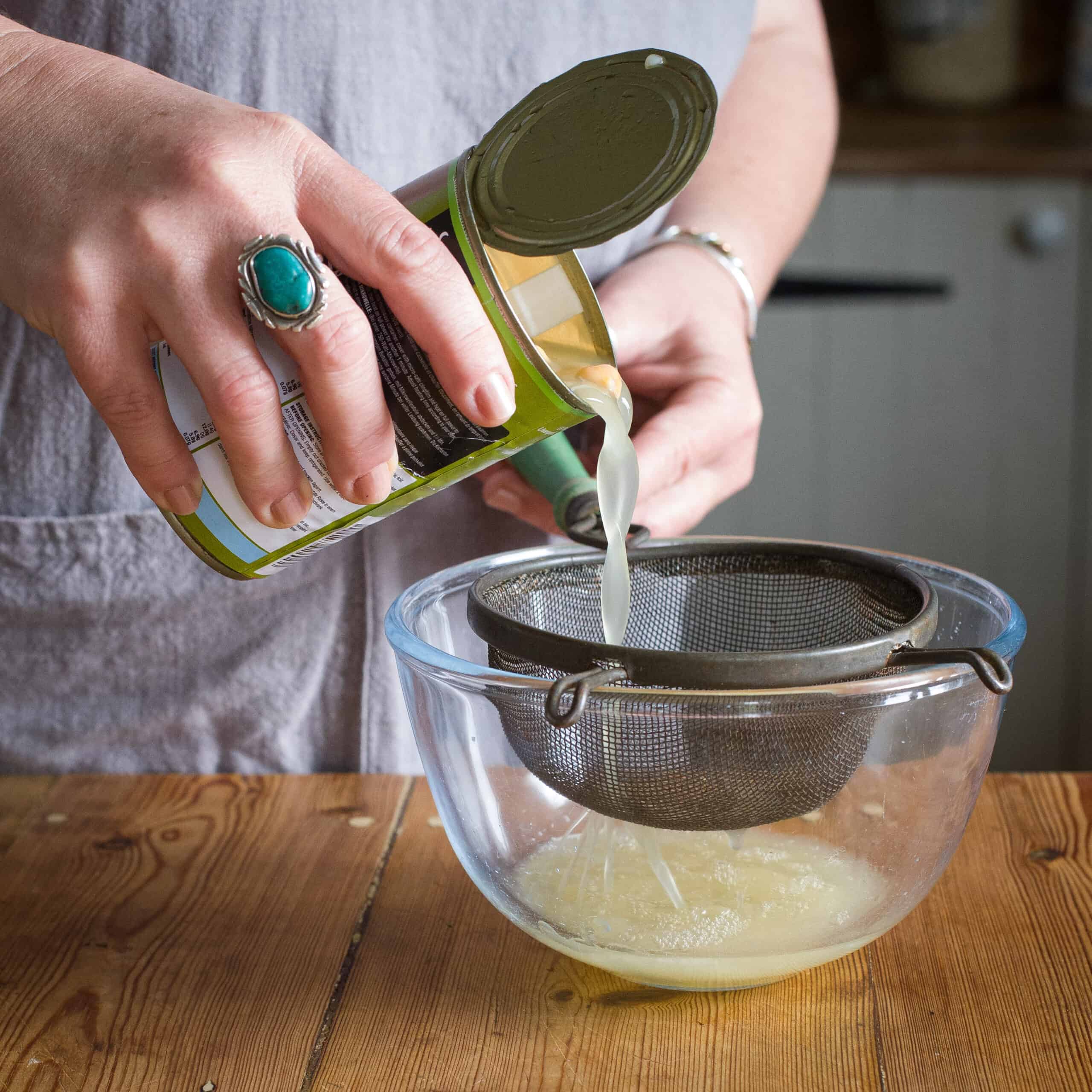 Woman’s hands pouring a can of chickpeas into a sieve over a glass bowl to drain off the liquid