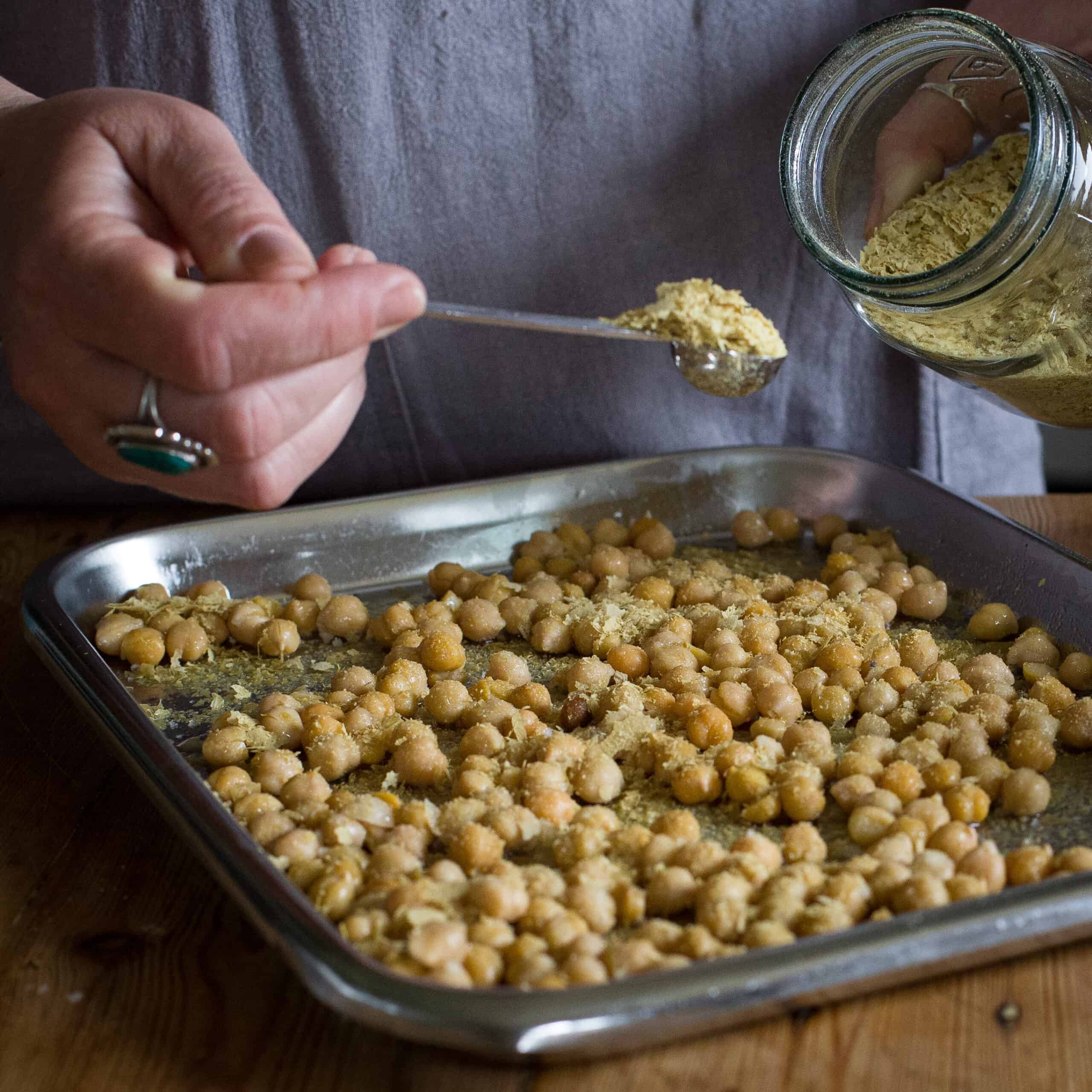 Woman’s hands sprinkling roasted chickpeas with nutritional yeast