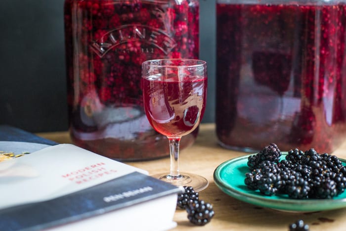 Blackberry Flavoured Vodka in a samall wine glass with 2 kilner jars a dish of blackberrys and a recipe book