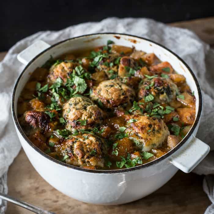 Ox Cheek Stew with Nettle Dumplings in a casserole dish on a wooden tavle with a cloth and serving spoon