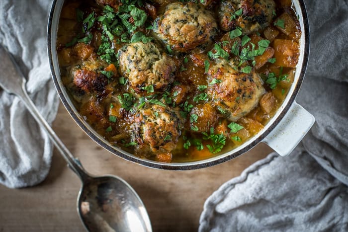 Ox Cheek Stew with Nettle Dumplings in a casserole dish on a wooden tavle with a cloth and serving spoon