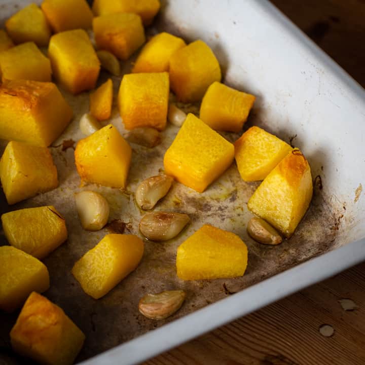 White enamel roasting tin with chucks of orange roast pumpkin and garlic cloves