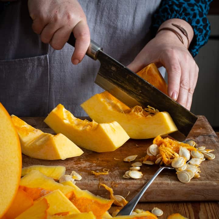 Woman’s hands slicing quarter of an orange pumpkin with a. Large Japanese knife