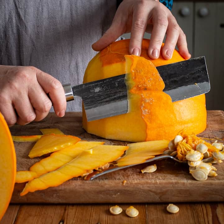 Woman’s hands slicing the skin from a large orange pumpkin