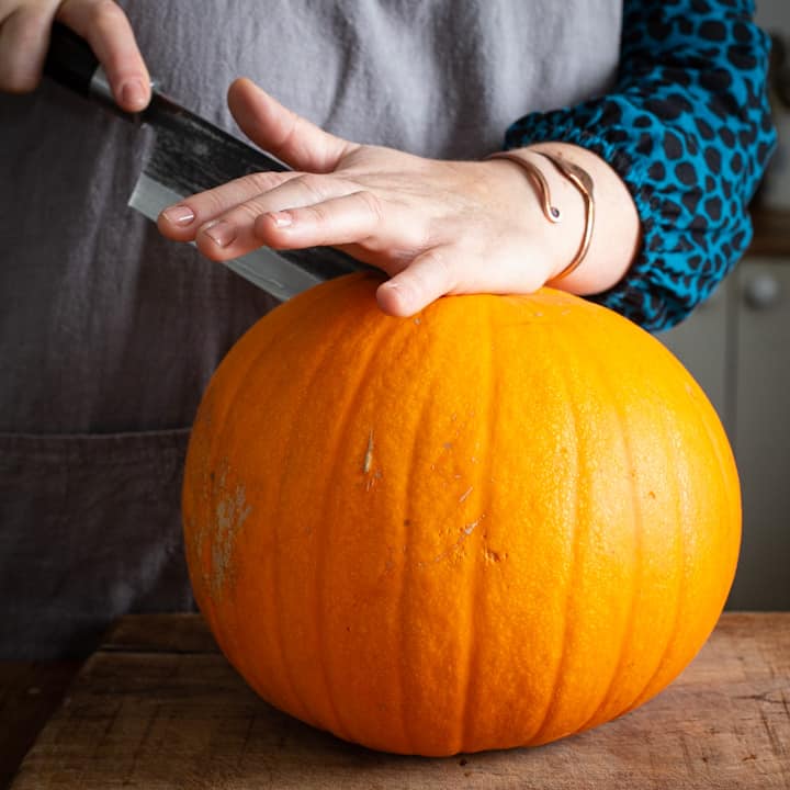 Woman in grey cutting into a pumpkin with a large Japanese knife