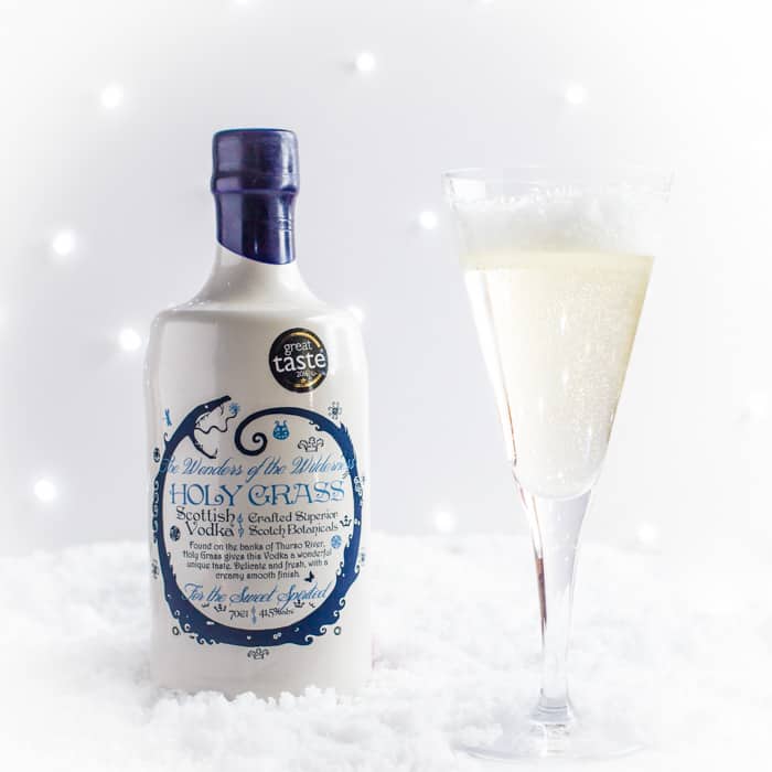 A bottle of Holy Grass Vodka and an Arctic Kiss vodka cocktail in a champagne flute on a bed of snow