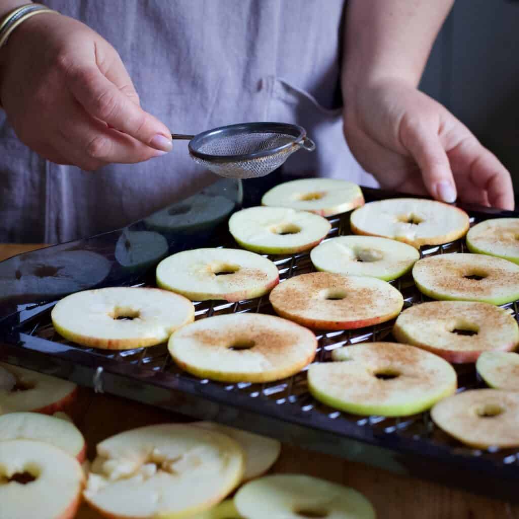 Woman sprinkled thin apple slices with cinnamon from a metal tea strainer