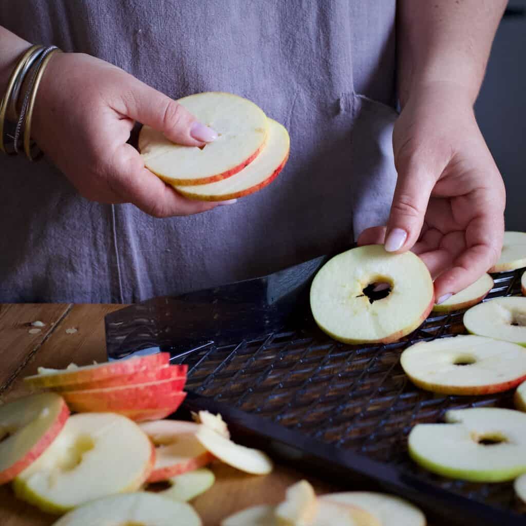 Woman in grey laying thin slices of apples onto a black plastic dehydrator shelf