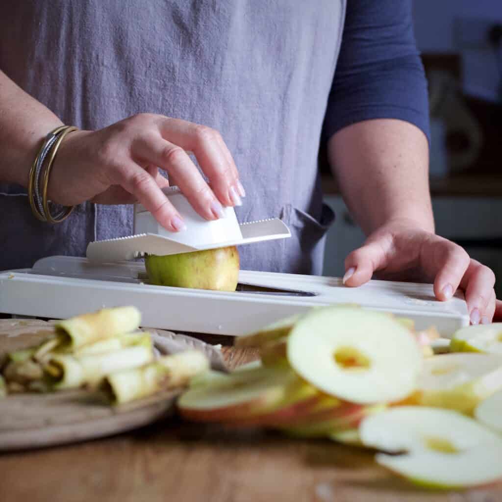 Woman slices apples into rings using a white plastic mandoline
