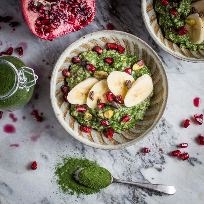 Bowl of pretty, bright green porridge made with DIY Green Superfood Powder, pomegranates, pistachios and banana