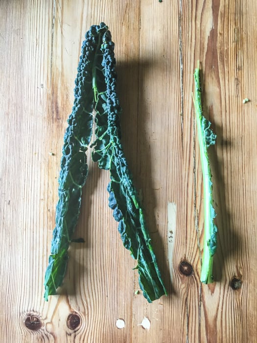 wooden counter with one kale leaf that has had the stem removed for dehydrating