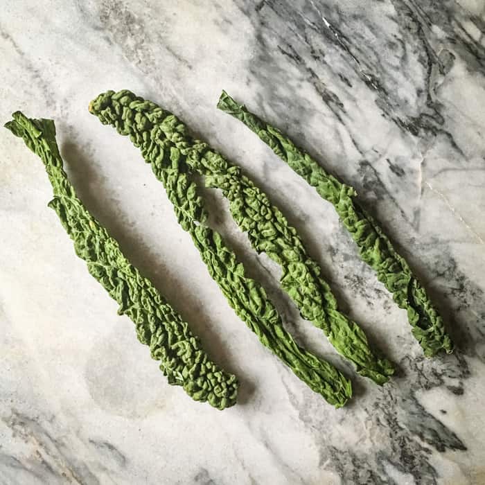 four dehydrated kale leaves on a marble slab