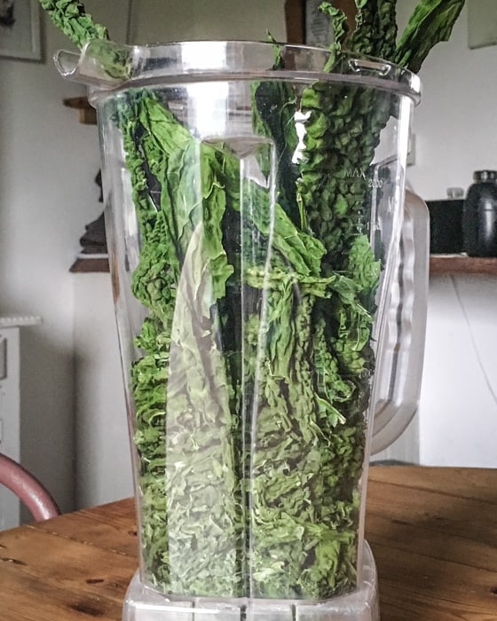 blender jug on wooden kitchen counter filled with dehydrated kale leaves