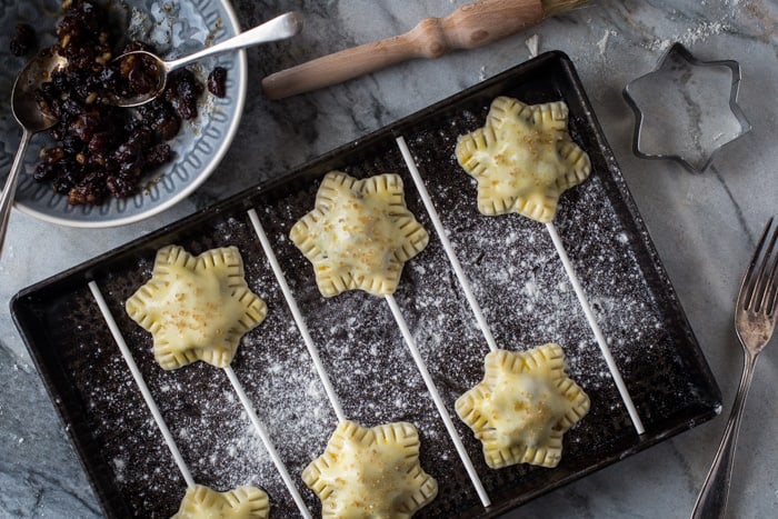 Mince Pie Pops in a baking tray sprinkled with icing sugar with a bowl of Mincemeat and baking equipment