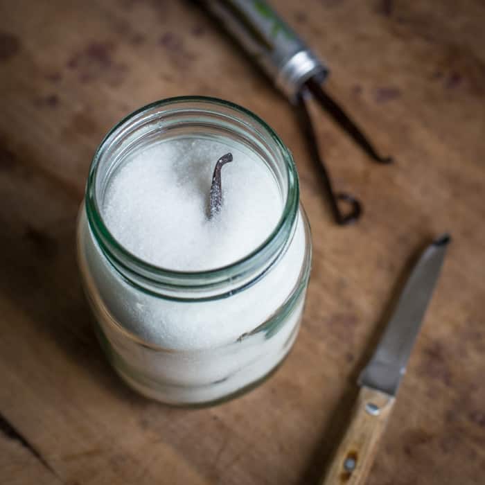 a glass jar of sugar with vanilla bean poking out of the top