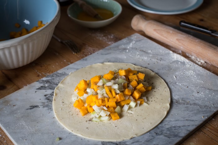 a disk of shortcrust pastry with the raw butternut and sage filling, ready to be crimped and baked