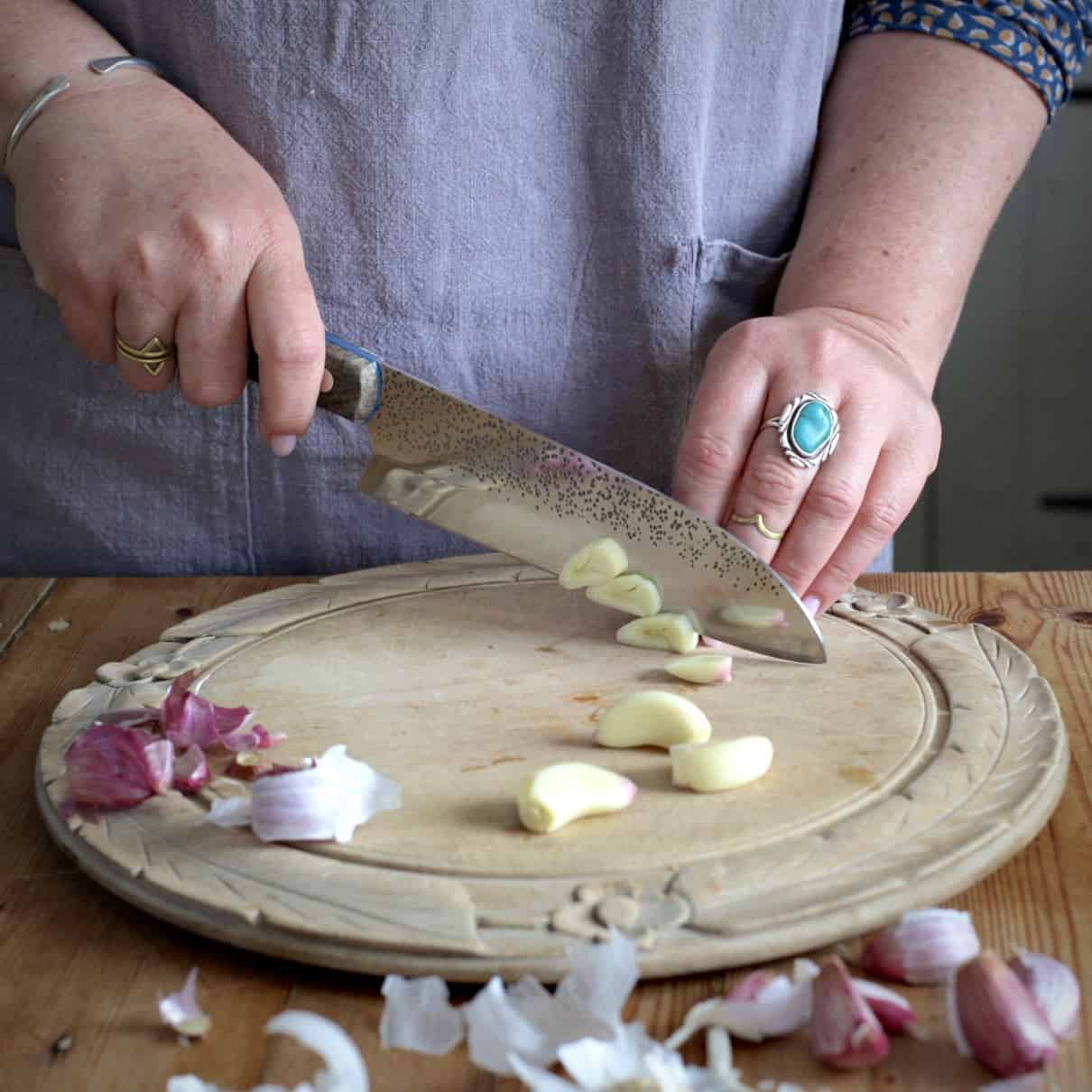 Woman in grey slicing garlic cloves on a old fashioned wooden chopping board