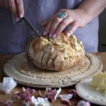 Woman in grey spreading garlic butter into a hedgehog sliced loaf of sourdough bread on a wooden board