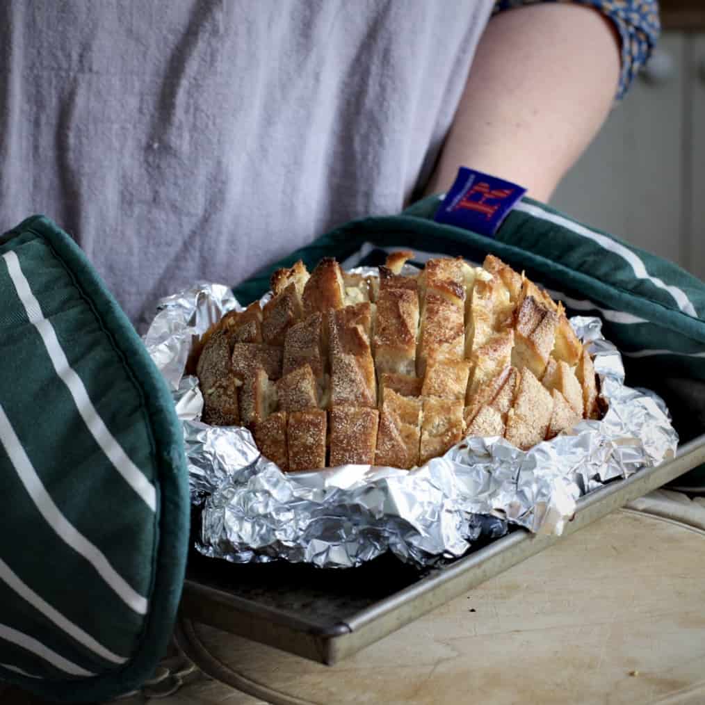 Woman holding a baking tray of hot baked garlic bread with green oven gloves