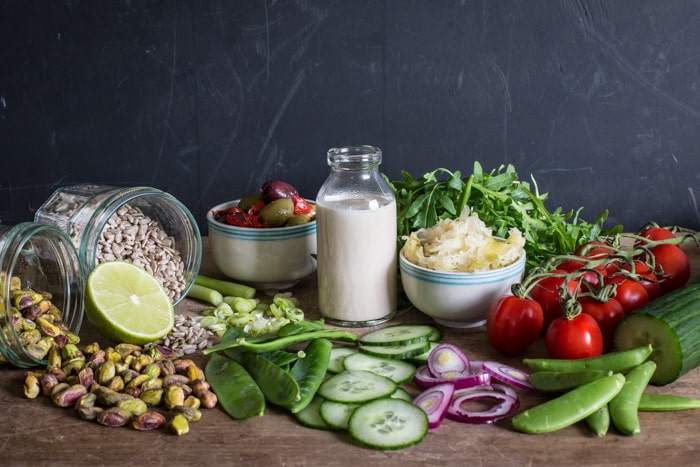 Small glass bottle of tahini sauce surrounded by a vibrant mix of salad vegetables, sauerkraut and olives