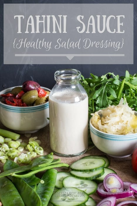 Small glass bottle of tahini sauce surrounded by a vibrant mix of salad vegetables, sauerkraut and olives