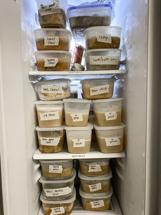 inside of a kitchen freezer with multiple plastic tubs full of nourishing homemade meals marked with masking tape and sharpie labels