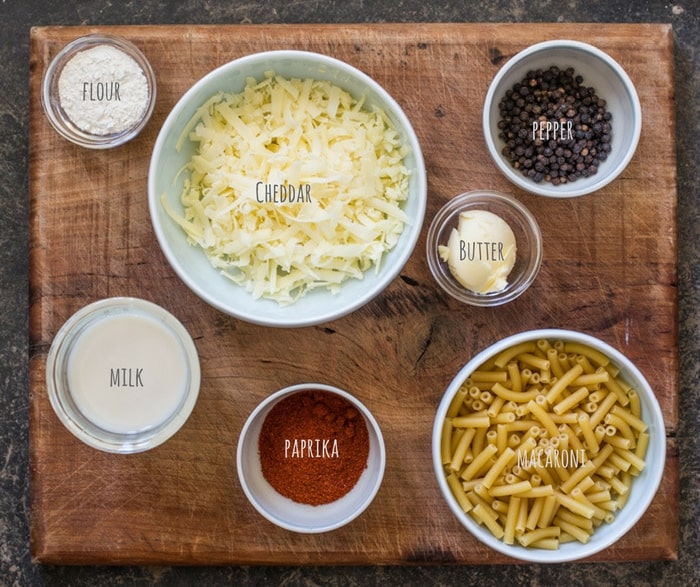 Ingredients for making a homemade mac and cheese in white bowls on a wooden board