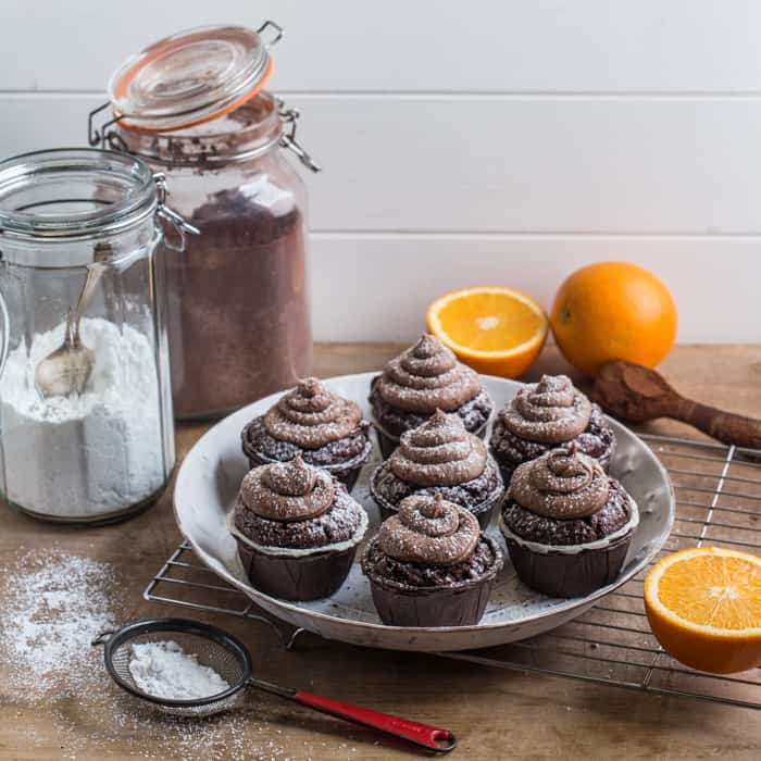 white plate with muffins and swirls of chocolate orange buttercream frosting, with jars of ingredients behind