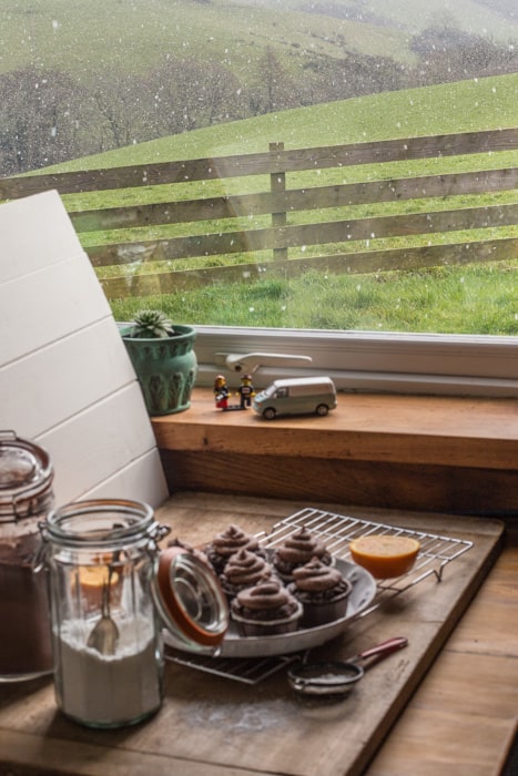 Mini photo studio next to window where muffins and swirls of chocolate orange buttercream frosting are being shot