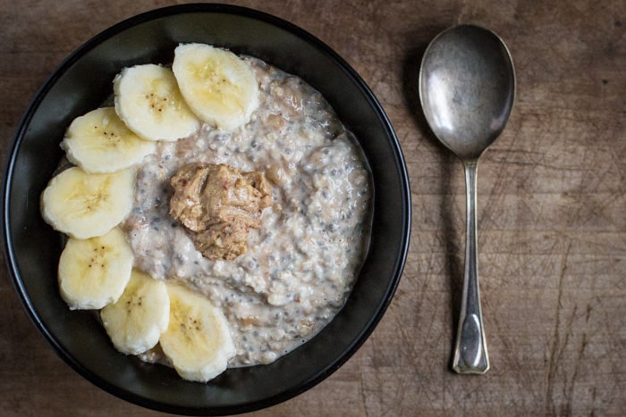 overnight oats with banana and peanut butter in a black bowl with a spoon on a table top