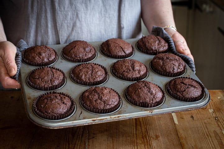 woman in grey holding a tray of fresh chocolate orange muffins