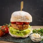 A tall sobrasada burger layered with lettuce, tomato and a wooden skewer holding it all together