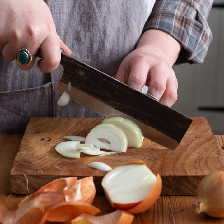 womans hands slicing a white onion on a wooden kitchen board