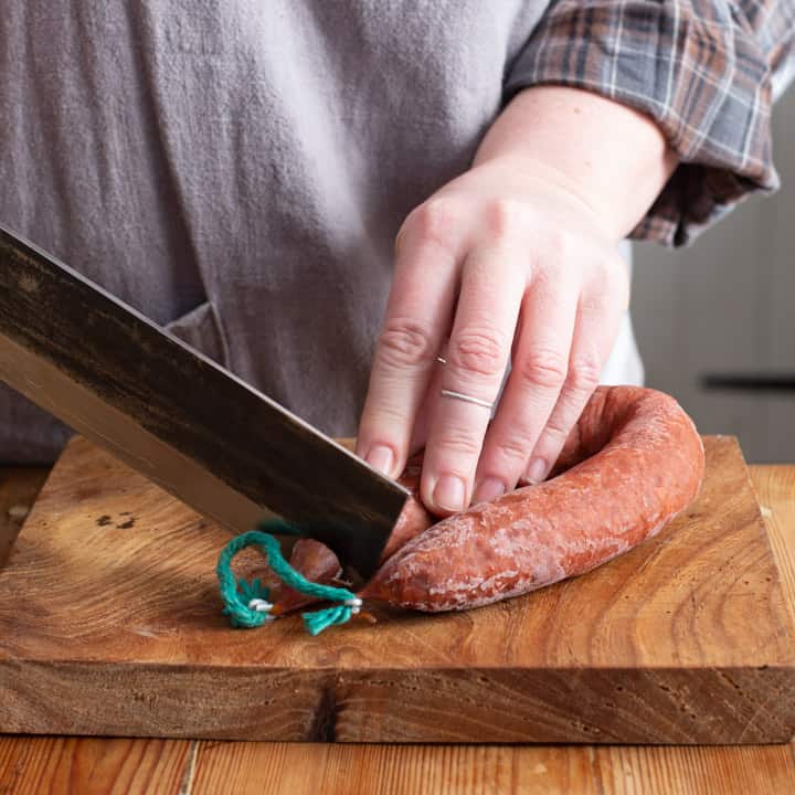 womans hands chopping a whole chorizo on a wooden board