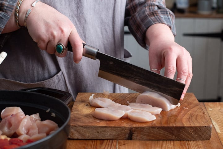 womans hands chopping chicken breasts on a wooden board