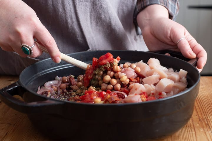 womans hands stirring the raw ingredients in a black pan of chicken chorizo and chickpea stew