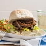 White bap stuffed with lettuce and juicy pulled lamb. on a white plate with salad and a small glass of wine in the background.