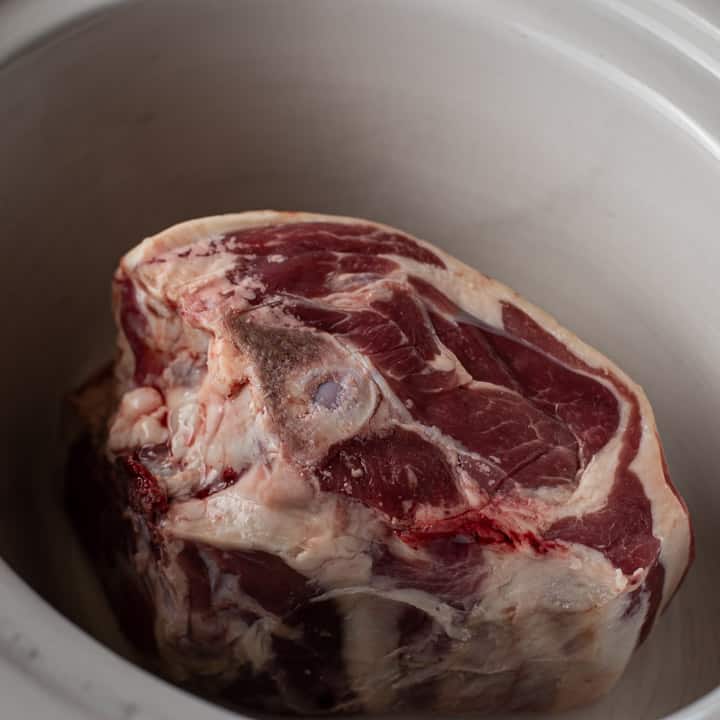 joint of lamb inside a white ceramic slow cooker