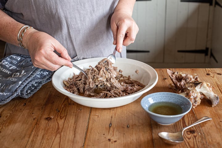 womands hands holding 2 forks and shredding tender pulled lamb apart