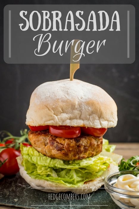 A tall sobrasada burger layered with lettuce, tomato and a wooden skewer holding it all together