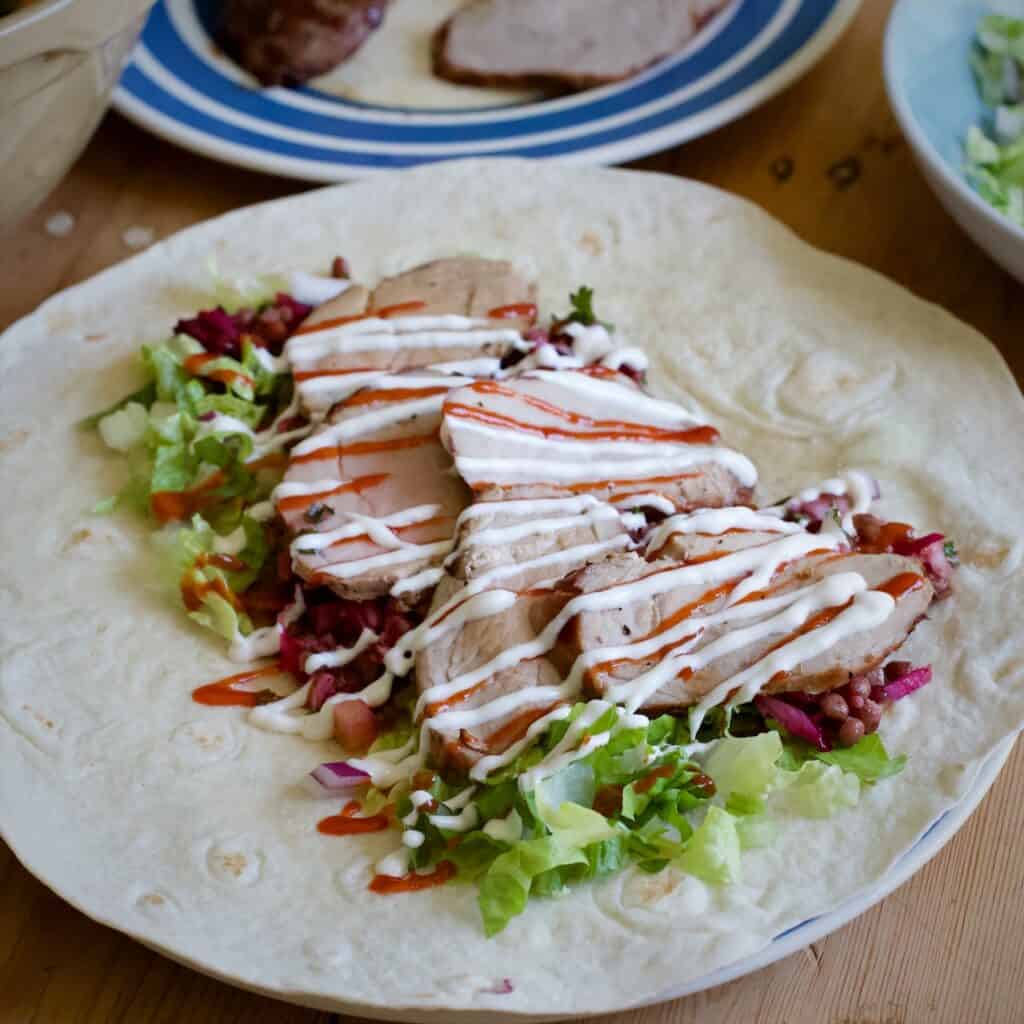 Slices of BBQ pork on a bed of salad and tortilla wrap drizzled with red and white sauce