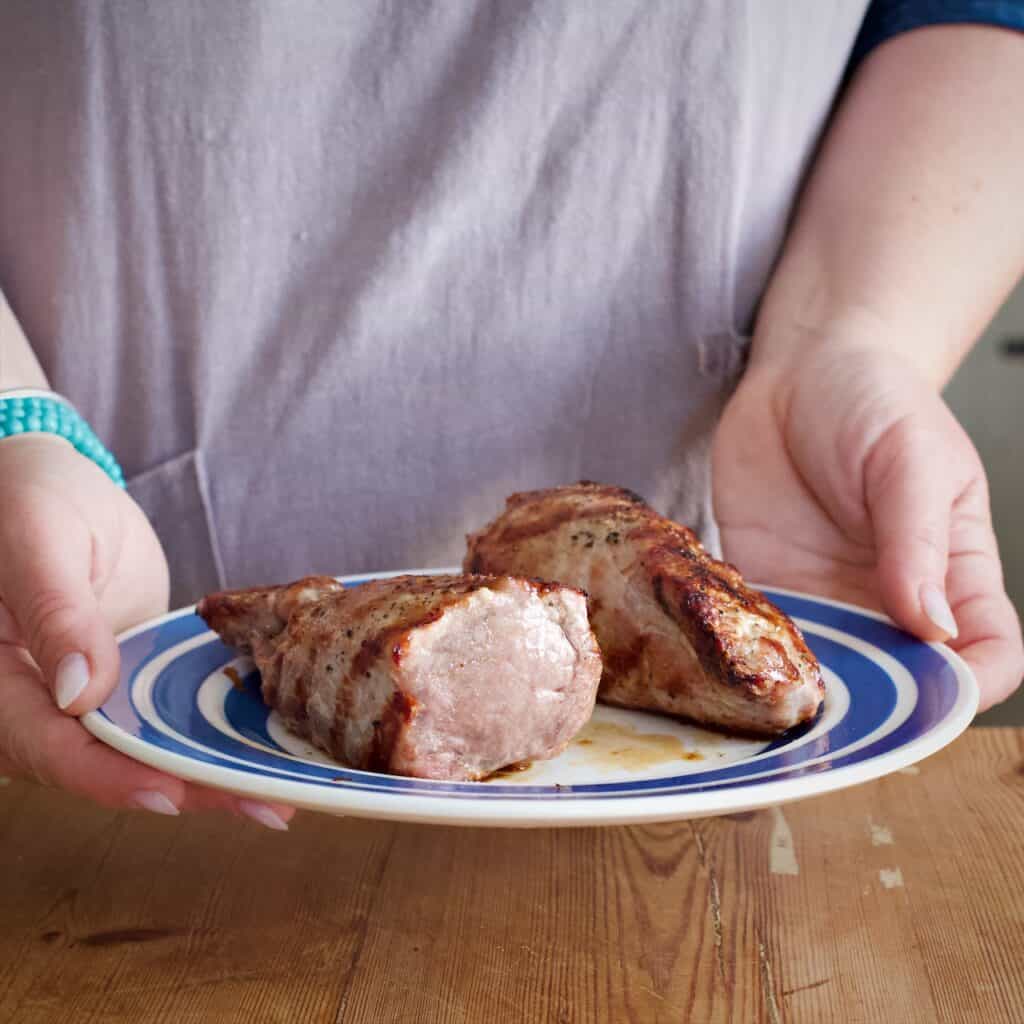 Woman holding blue and white plate with two cooked pieces of BBQ pork fillet