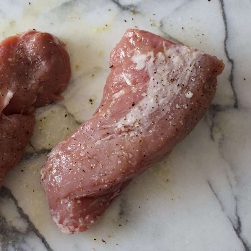 Two pieces of seasoned pork tenderloin on a marble slab ready to go on the BBQ