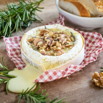 Molten baked Camembert cheese melting out of its wooden tub with rosemary and walnuts all on a wooden board