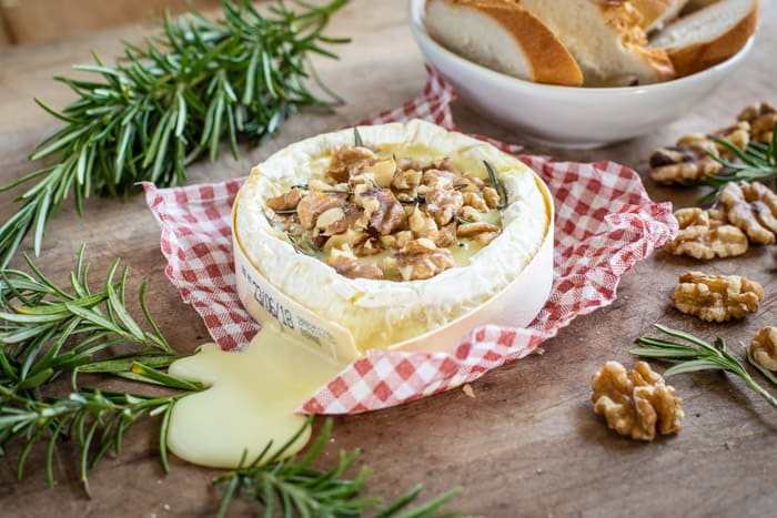 Molten BBQ Camembert cheese melting out of its wooden tub with rosemary and walnuts all on a wooden board