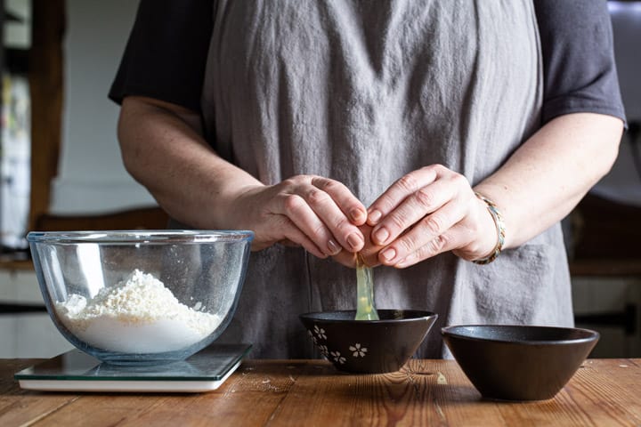 womans hands cracking an egg into a small black bowl on a wooden kitchen counter