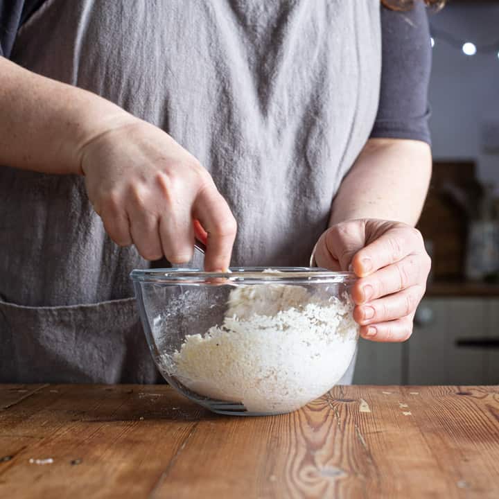 womans hands mixing white ingredients in a glass bowl on a wooden kitchen counter